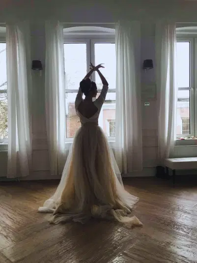  Ballerina w eleganckiej sukni balowej tańczy w jasnym pokoju z dużymi oknami. 