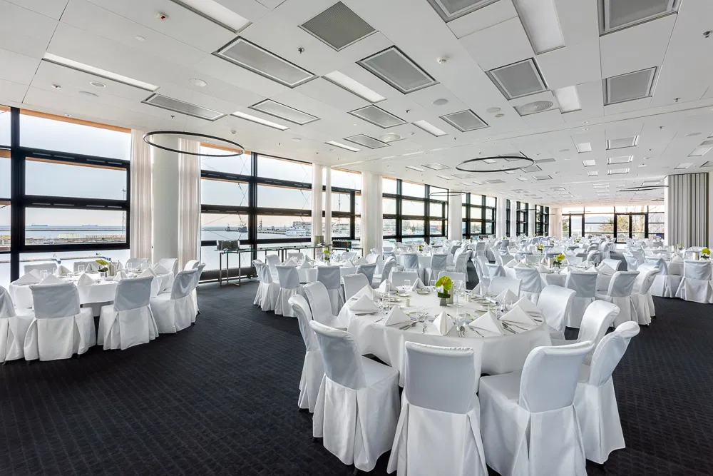 Elegancka sala bankietowa z okrągłymi stołami, przygotowana na wydarzenie z widokiem na port.