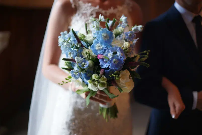  Panna młoda trzymająca bukiet ślubny z niebieskimi i białymi kwiatami, elegancka suknia z koronką, ślub w romantycznym stylu. 