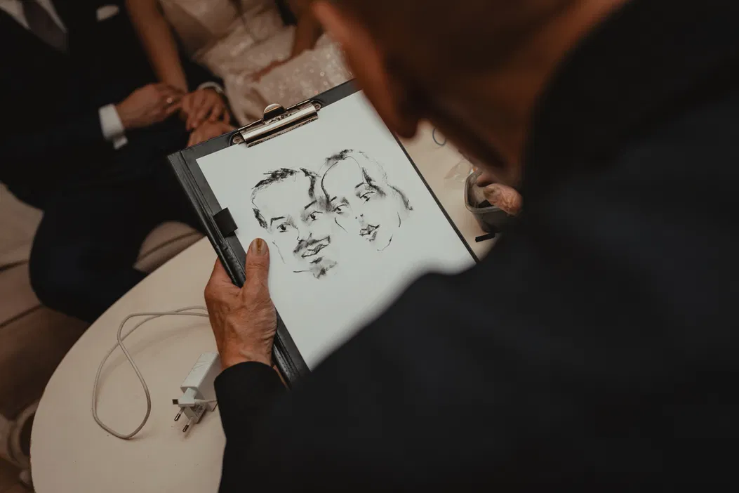 Osoba szkicująca portret pary siedzącej na sofie w eleganckich strojach.