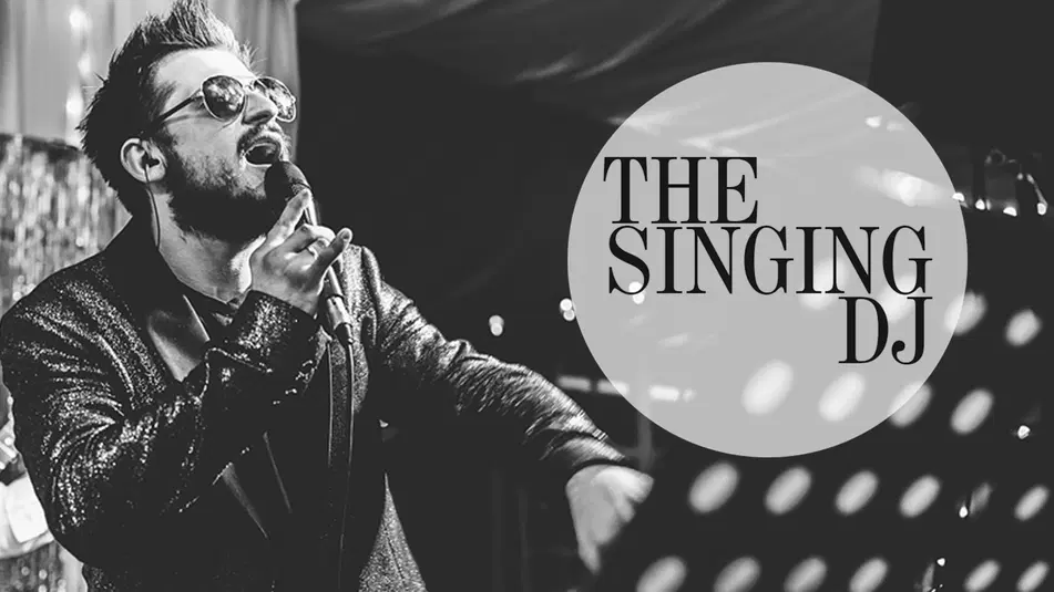  Czarnobiała fotografia śpiewającego DJ-a w okularach, trzymającego mikrofon, z napisem The Singing DJ obok niego; sceniczne oświetlenie i błyszcząca marynarka dodają dynamiki zdjęciu. 