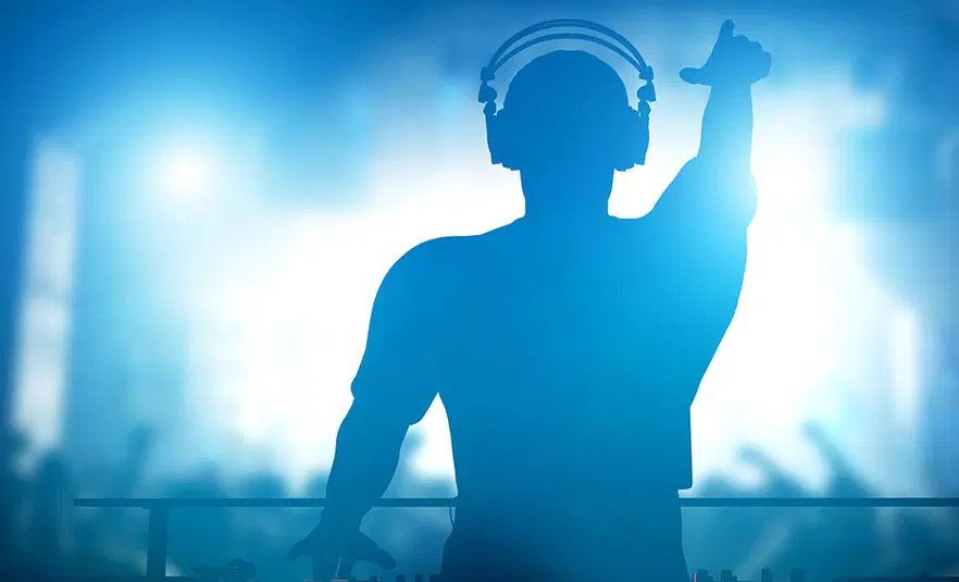  DJ miksujący muzykę na żywo na konsolecie w klubie nocnym, widzowie tańczący w tle. 