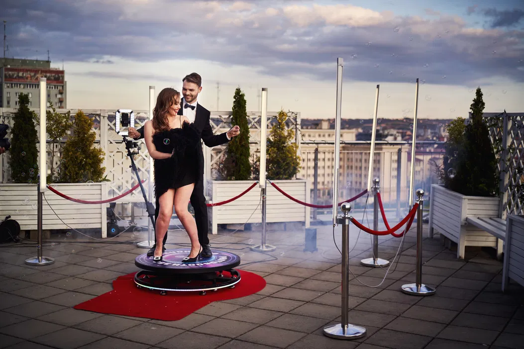 Para tańcząca na tarasie z panoramą miasta w tle, czerwony dywan, eleganckie stroje, atmosfera luksusu i elegancji.