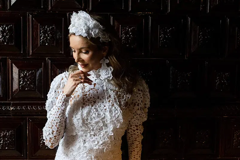  Biała sukienka koronkowa na tle drewnianej ściany, elegancka moda ślubna, stylizacja ślubna z ozdobną opaską, detale koronki. 