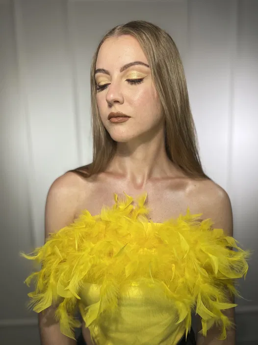 Moda kobieca, żółty top z piórami, makijaż w odcieniach złota, elegancki styl.
