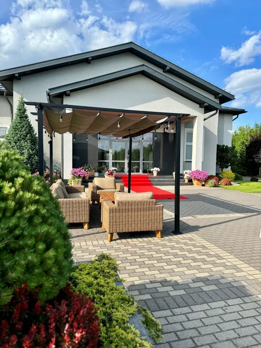 Nowoczesny dom z zewnętrznym tarasem, elegancką architekturą i ogrodem, który idealnie komponuje się z czerwoną wykładziną prowadzącą do wejścia.
