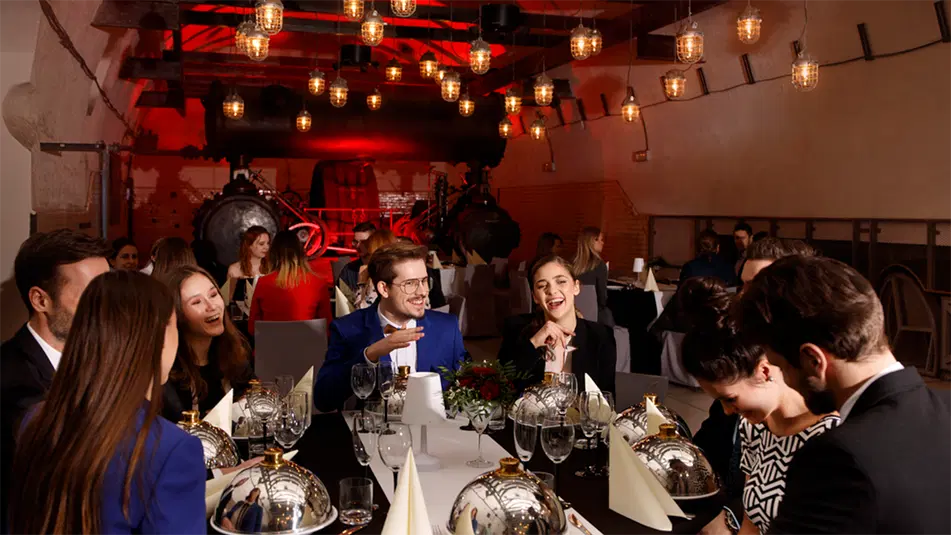  Spotkanie towarzyskie w eleganckiej restauracji, śmiejący się ludzie przy stole, nowoczesne oświetlenie, industrialna dekoracja wnętrza. 
