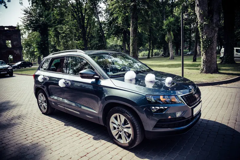  Samochód SUV ozdobiony na ślub, stojący na brukowanej drodze w parku z drzewami w tle. 