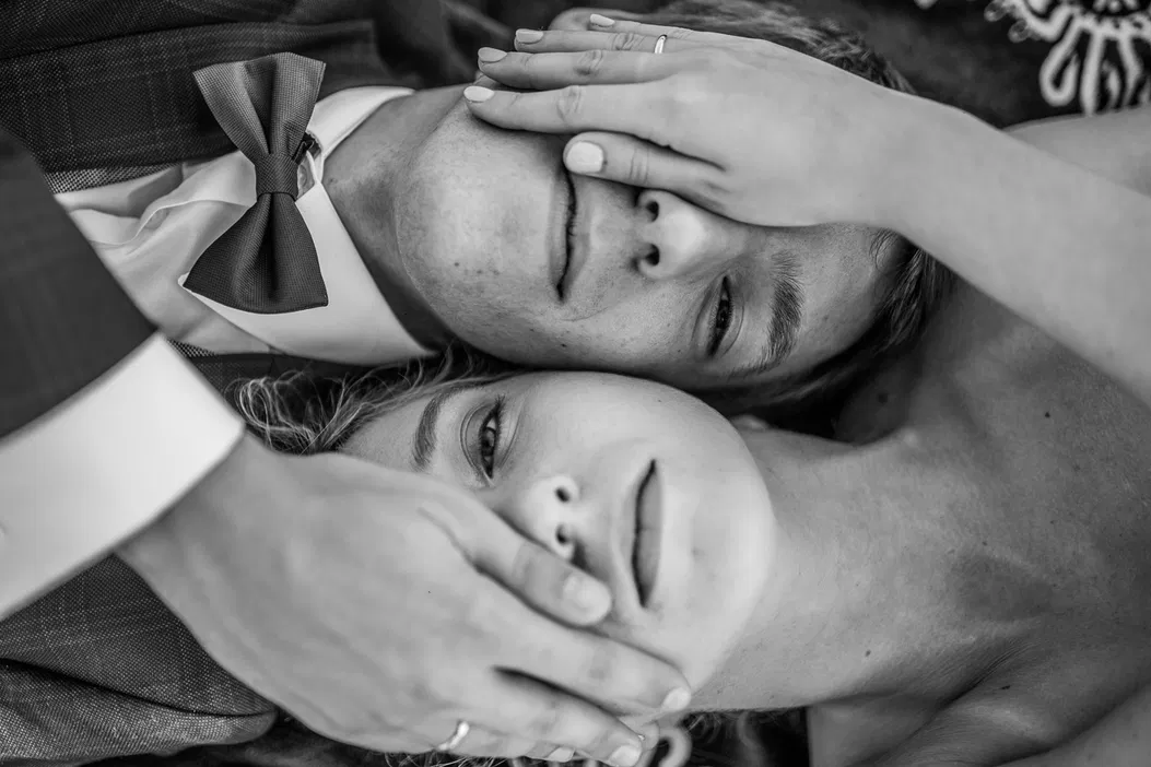 Czarno-białe zdjęcie romantyczne pary leżącej razem, twarze blisko siebie, mężczyzna w muszce, kobieta z ręką zakrywającą twarz partnera.