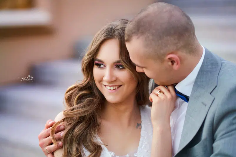  Young couple embracing, woman in white dress smiling, close-up shot, outdoor romantic setting. 