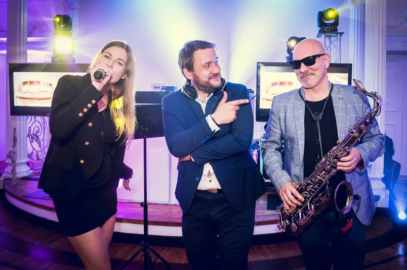  Muzyczny występ na żywo: wokalistka z mikrofonem, DJ w słuchawkach i saksofonista na eleganckiej imprezie. 