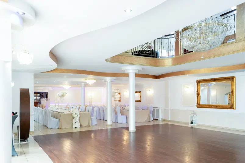  Sala weselna z eleganckim wystrojem, duży kryształowy żyrandol, białe obrusy, dekoracje kwiatowe, luksusowa atmosfera. 