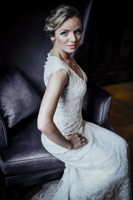Elegancka panna młoda w koronkowej sukni ślubnej siedząca na krześle w ciemnym otoczeniu