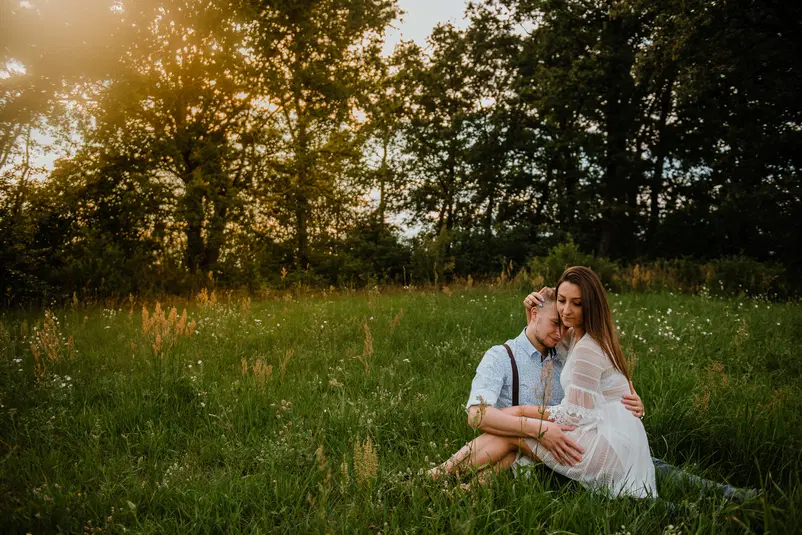  Para siedząca na zielonej łące o zachodzie słońca, otoczona drzewami, romantyczna fotografia w plenerze. 