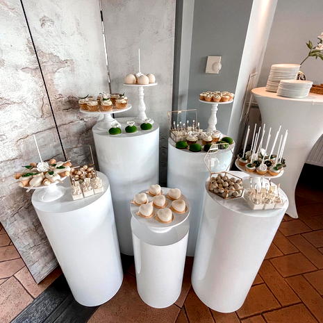  Dekoracyjny stół weselny z eleganckimi białymi i zielonymi deserami, w tym babeczki i cake popsy na stylowych białych podestach. 