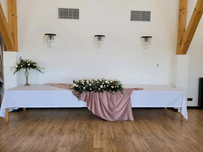  Dekoracja sali weselnej z kwiatami i różowym materiałem na białym stole, drewniana podłoga, nowoczesne wnętrze. 