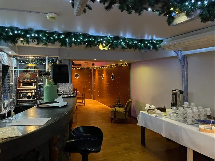  Elegancki wystrój wnętrza restauracji z ozdobami świątecznymi na suficie, stolikiem z filiżankami i naczyniami, barem z szklankami oraz nastrojowym, ciepłym oświetleniem. 