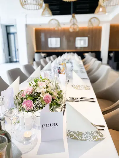  Elegancko udekorowany stół w restauracji z bukietem kwiatów i złożonymi serwetkami, przygotowany na przyjęcie lub spotkanie okolicznościowe. 