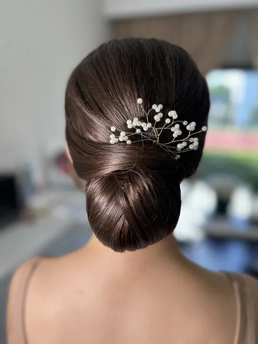 Elegancka fryzura upięcie na ślub z ozdobą z perłami na włosach brązowych.