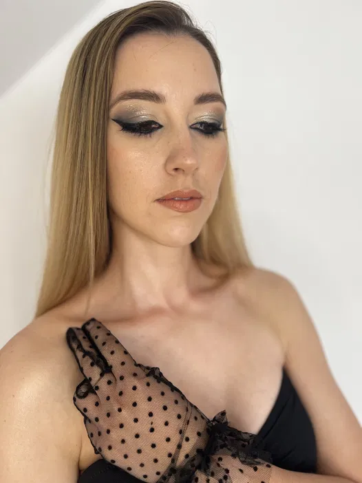 Kobieta w eleganckim makijażu z czarnym tiulowym rękawem w czarne kropki, spoglądająca w dół, z rozpuszczonymi blond włosami na białym tle