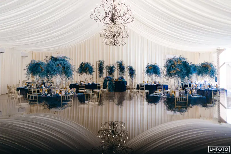  Elegancka sala weselna z ozdobnymi niebieskimi dekoracjami i złotymi krzesłami, gotowa na przyjęcie. 