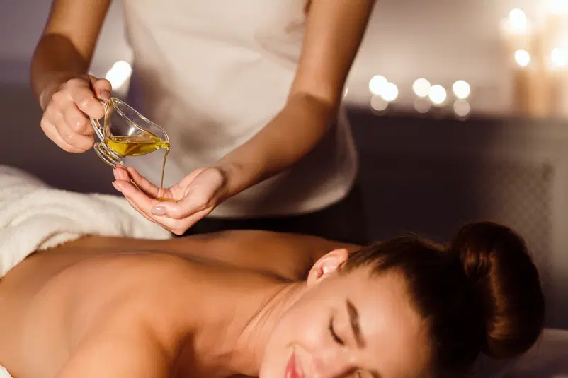  Masaż relaksacyjny z użyciem olejków eterycznych w spa, kobieta leżąca na stole do masażu, w tle zapalone świece. 