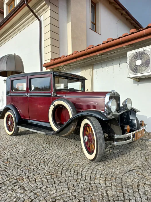 Zabytkowy samochód retro na tle budynku, klasyczny pojazd z początku XX wieku, elegancki model z białymi oponami na bruku.