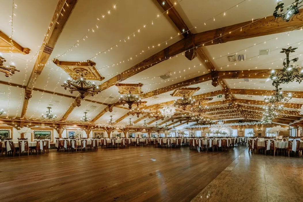 Elegancka sala bankietowa z ozdobnym oświetleniem i drewnianym wystrojem wnętrza, przygotowana na przyjęcie weselne.