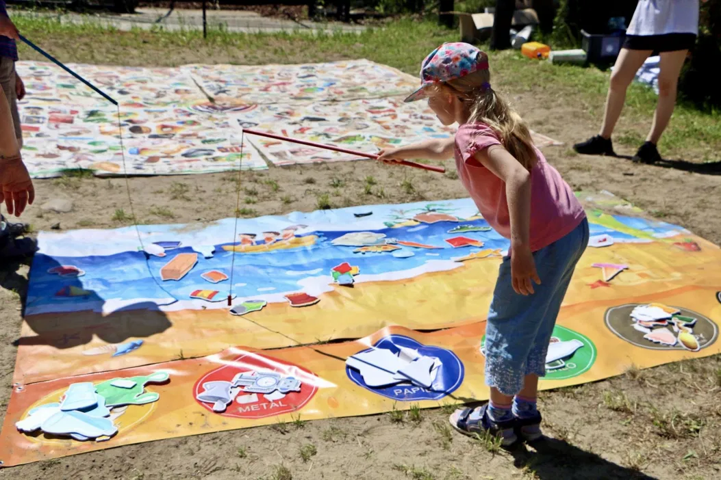 Dziewczynka bawiąca się na świeżym powietrzu na grach edukacyjnych z elementami recyklingu i ochrony środowiska, kolorowe maty do zabawy, letnia pogoda.