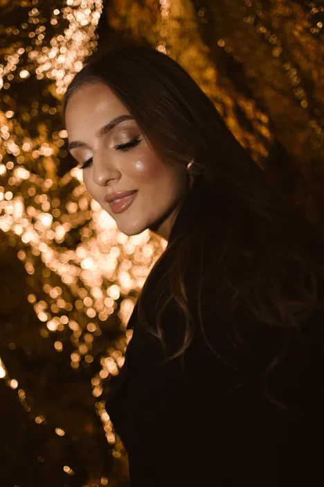 Portret kobiety z zamkniętymi oczami na tle złotych świateł bokeh, elegancki makijaż glamour.