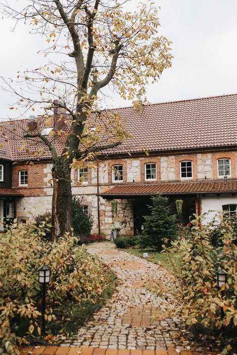 Zabytkowy dom z ceglaną fasadą i brukowaną ścieżką, otoczony jesienną roślinnością.