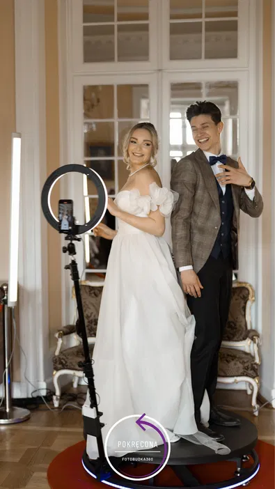 Para młoda pozująca na sesji zdjęciowej z fotobudką 360, elegancka suknia ślubna, garnitur, wesele, nowoczesna fotografia, sprzęt fotograficzny, wnętrze z dużym lustrem i eleganckimi meblami.