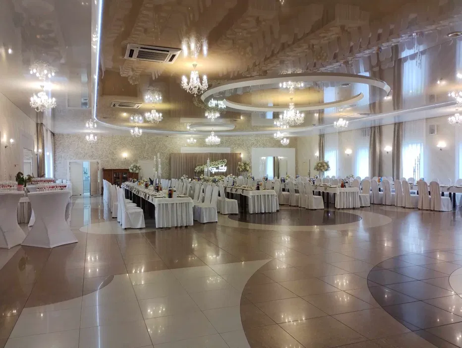 Elegancka sala bankietowa z dekoracyjnymi żyrandolami, ustawione stoły na przyjęcie, białe krzesła, luksusowy wystrój wnętrza.