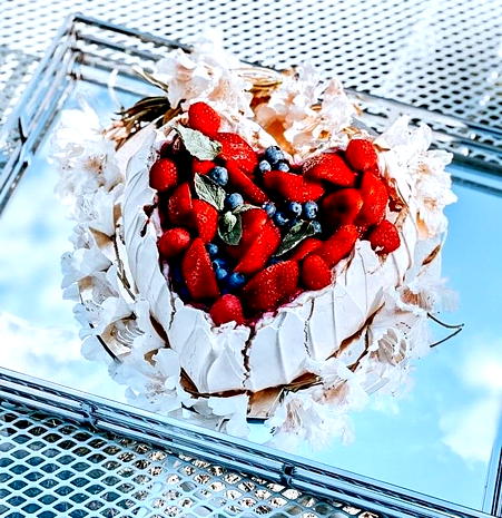  Tort bezowy w kształcie serca z truskawkami i jagodami na szklanym talerzu, udekorowany miętą, idealny deser na lato. 