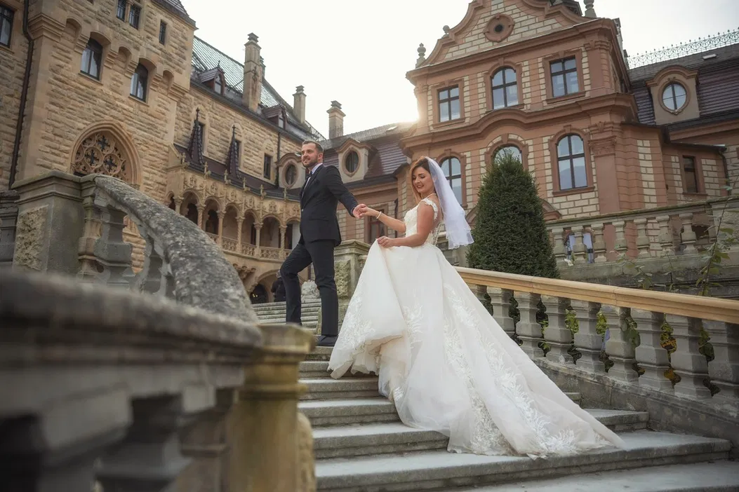 Para młoda na schodach zamku podczas sesji ślubnej, panna młoda w białej sukni, pan młody w eleganckim garniturze, romantyczna sceneria.