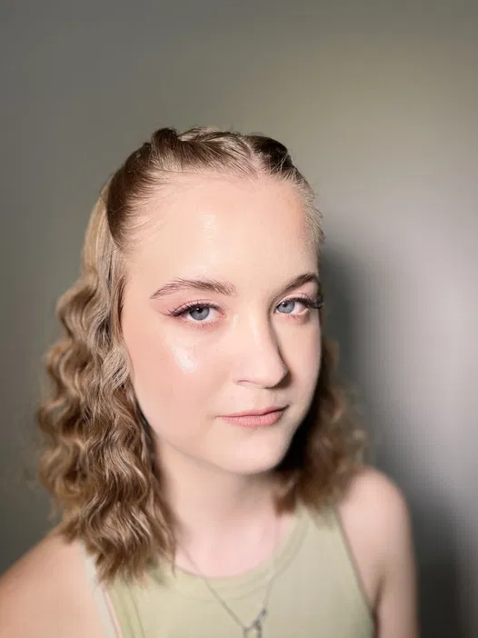 Młoda kobieta o blond kręconych włosach na białym tle, ubrana w zielony top.