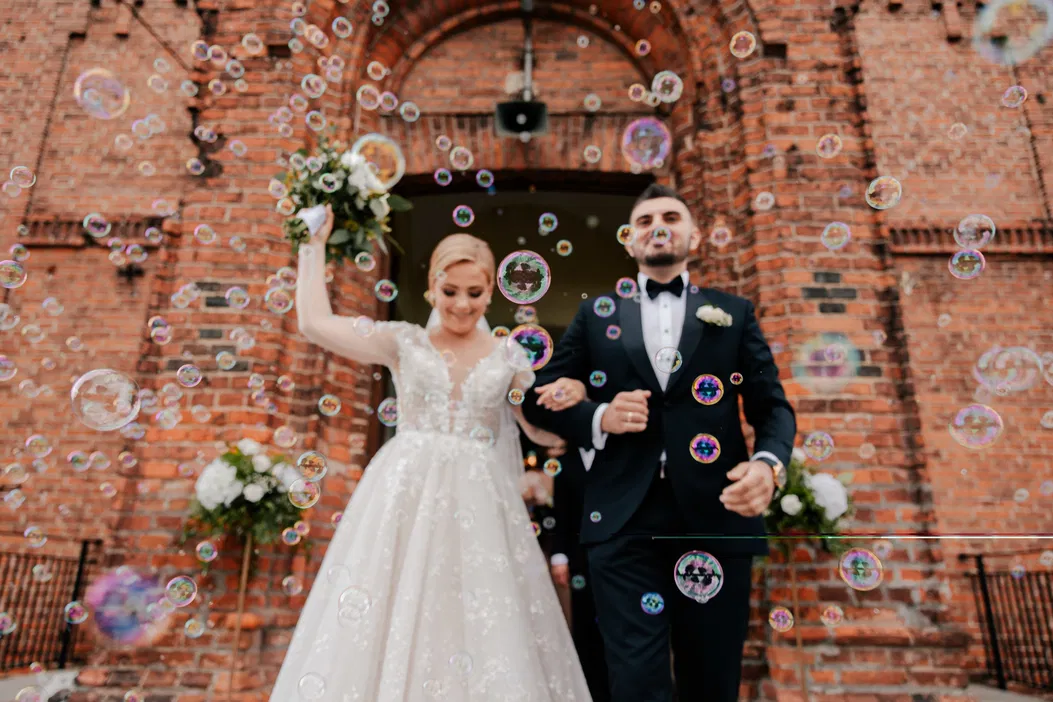 Para młoda wychodząca z kościoła, otoczona bańkami mydlanymi, suknia ślubna, garnitur, romantyczny moment, szczęśliwa ceremonia ślubna.