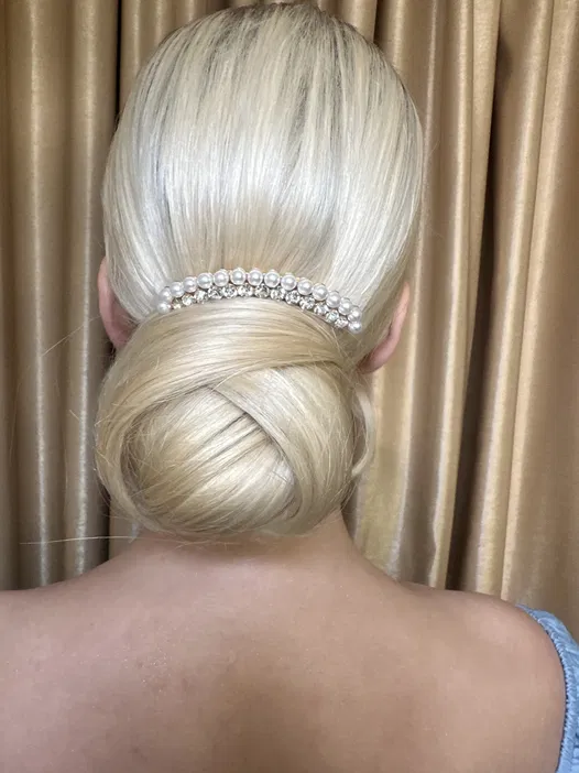 Upięcie włosów blond z ozdobną spinką z perełkami i kryształkami na tle beżowej tkaniny.