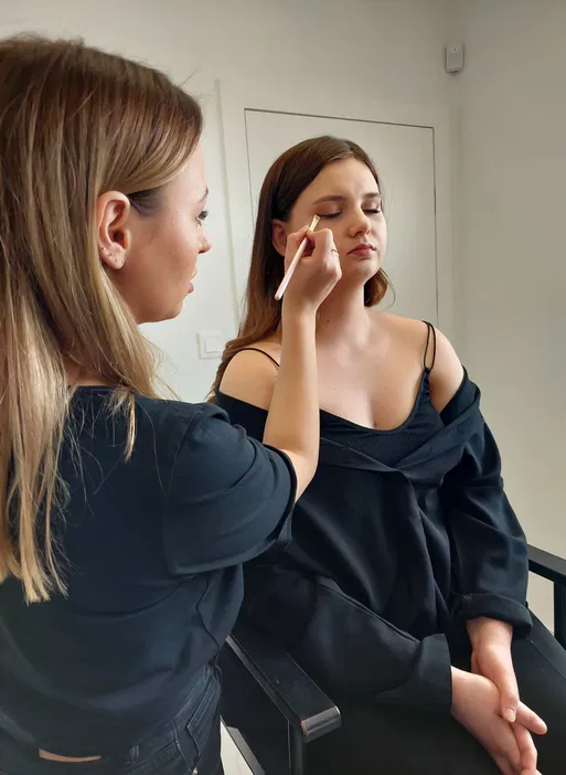 Makijażystka nakłada makijaż u modelki w salonie kosmetycznym, profesjonalne usługi make-up.