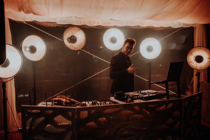  DJ na imprezie z efektownym oświetleniem, scena DJ-ska z konsolą i laptopem, klimatyczna atmosfera muzyczna. 