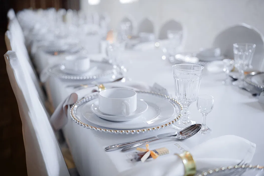 Elegancko nakryty stół bankietowy z białą zastawą i zdobionymi talerzami, przygotowany na uroczyste przyjęcie.