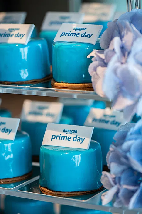 Niebieskie ciastka z logo Amazon Prime Day na tacy, dekorowane kwiatami. Idealne na promocję wydarzenia zakupowego.
