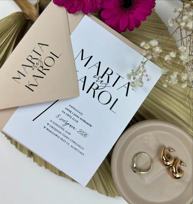 Niestandardowe zaproszenia ślubne Marta i Karol z eleganckimi dodatkami, obrączką i złotymi kolczykami, stylizacja boho z kwiatami i elementami dekoracyjnymi.
