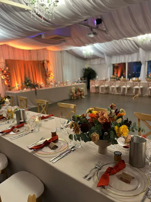 Dekoracja sali weselnej z elegancko nakrytymi stołami, świeżymi kwiatami w jesiennych kolorach i subtelnym oświetleniem na aranżacji przyjęcia.