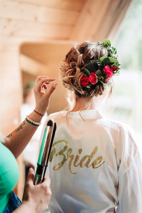 Panna młoda przygotowująca się do ślubu, fryzura z kwiatami, szlafrok z napisem Bride.