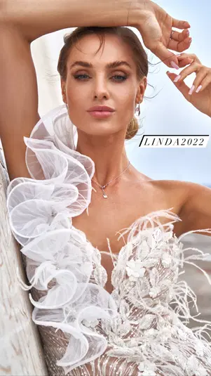  Modelka w eleganckiej sukni ślubnej z koronkowymi detalami i falbanami, pozująca w plenerze. 