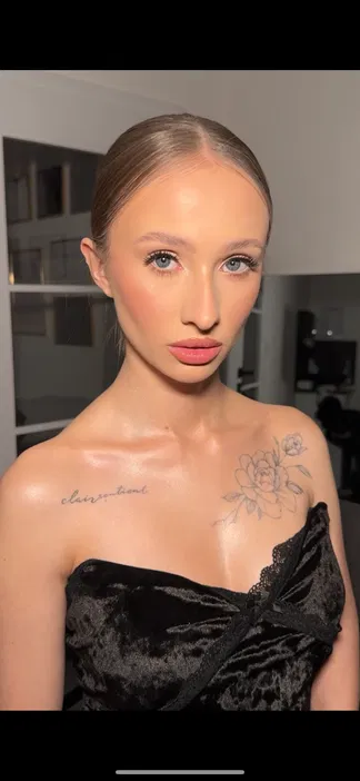 Portret młodej kobiety z eleganckim makijażem i tatuażem na ramieniu, ubranej w czarną aksamitną sukienkę.