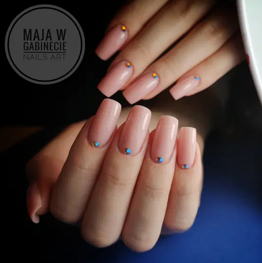  Eleganckie paznokcie żelowe z jasnoróżowym lakierem i delikatnymi ozdobami, manicure salonu Maja w Gabinecie. 