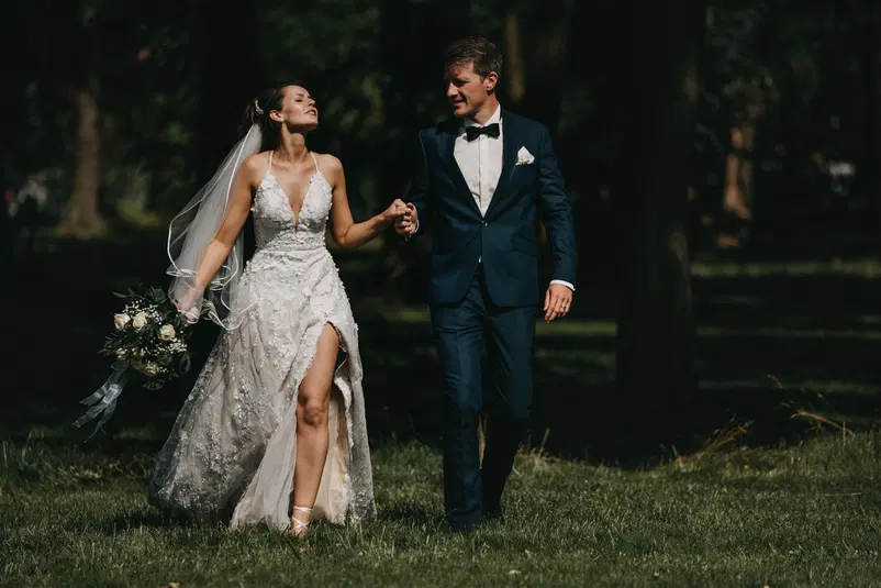  Para młoda na romantycznej sesji ślubnej w parku, panna młoda w koronkowej sukni i pan młody w eleganckim garniturze, zielone otoczenie. 