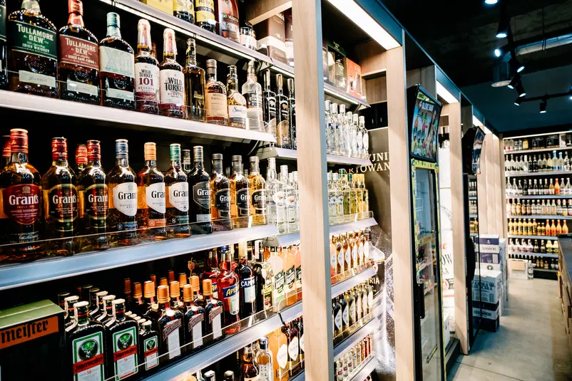  Regały z alkoholem w sklepie, różne marki whiskey i likierów, zróżnicowana oferta butelek w jasnym oświetleniu. 